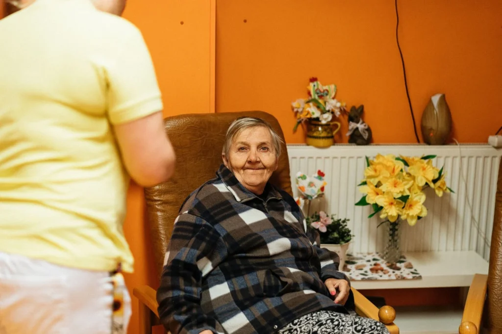 Cuidadora ao lado de uma idosa sorrindo na sala de casa