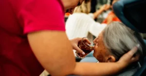 Cuidadora ampara e dá de beber a uma idosa em casa