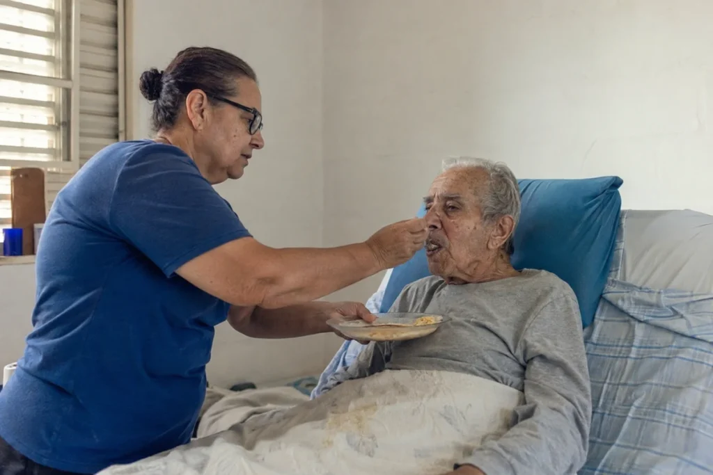 Cuidadora oferecendo comida a um idoso acamado sentado na cama