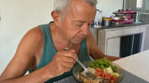 Idoso comendo peixe rico em ômega 3, com arroz e salada, à mesa em casa